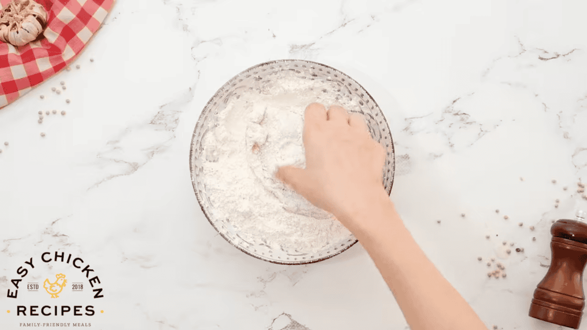 dipping a buttermilk-coated raw chicken breast in flour.