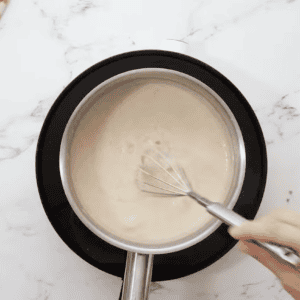 seasoned thickened white gravy in a saucepan with a whisk.
