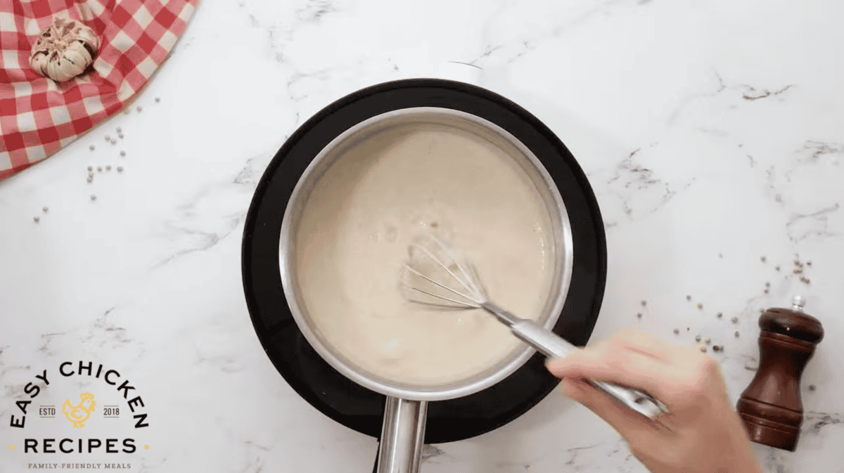 seasoned thickened white gravy in a saucepan with a whisk.