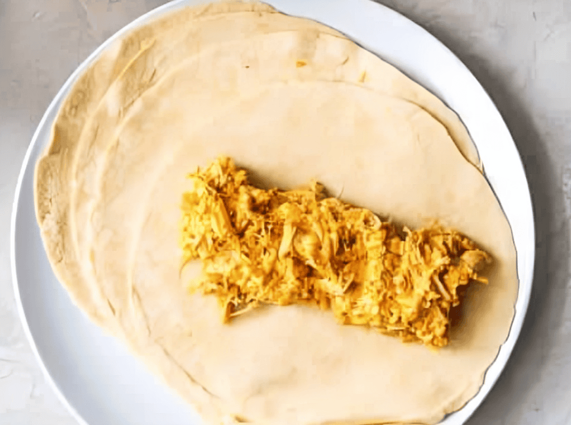 buffalo chicken enchilada filling laid in a log on top of a flour tortilla.