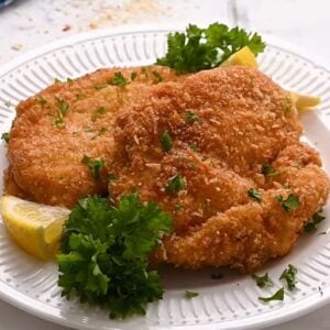 Chicken schnitzel on a plate with lemon wedges and fresh parsley