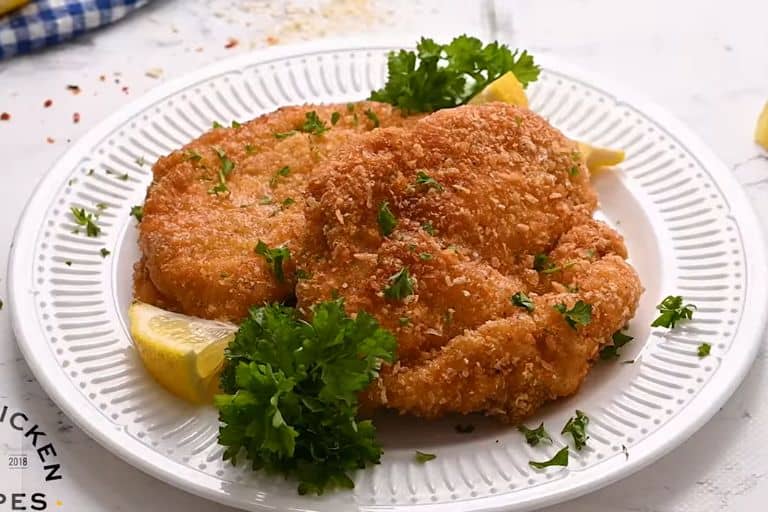 Chicken schnitzel on a plate with lemon wedges and fresh parsley