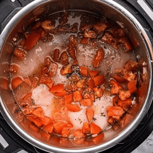 raw chicken breasts topped with seasonings, broth, and chopped tomatoes in an instant pot.