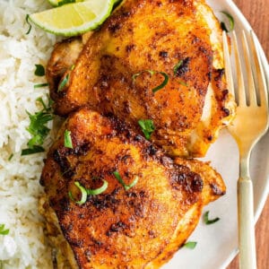 overhead image of crispy air fryer chili lime chicken thighs on a plate with rice and lime wedges.