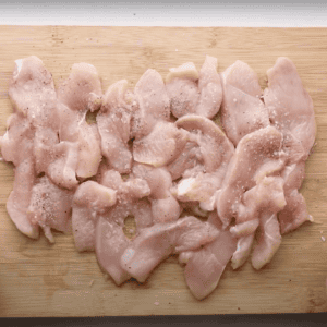 seasoned raw sliced chicken on a cutting board.