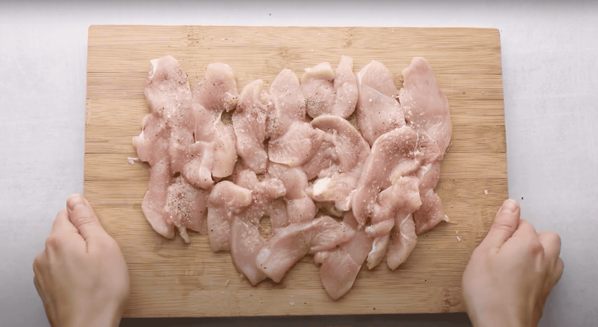 seasoned raw sliced chicken on a cutting board.
