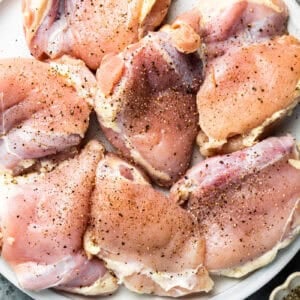 raw seasoned chicken thighs on a white plate.