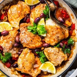 overhead view of chicken provencal in a brasier with lemon wedges.