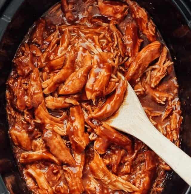 bbq chicken in a slow cooker with a wooden spoon.