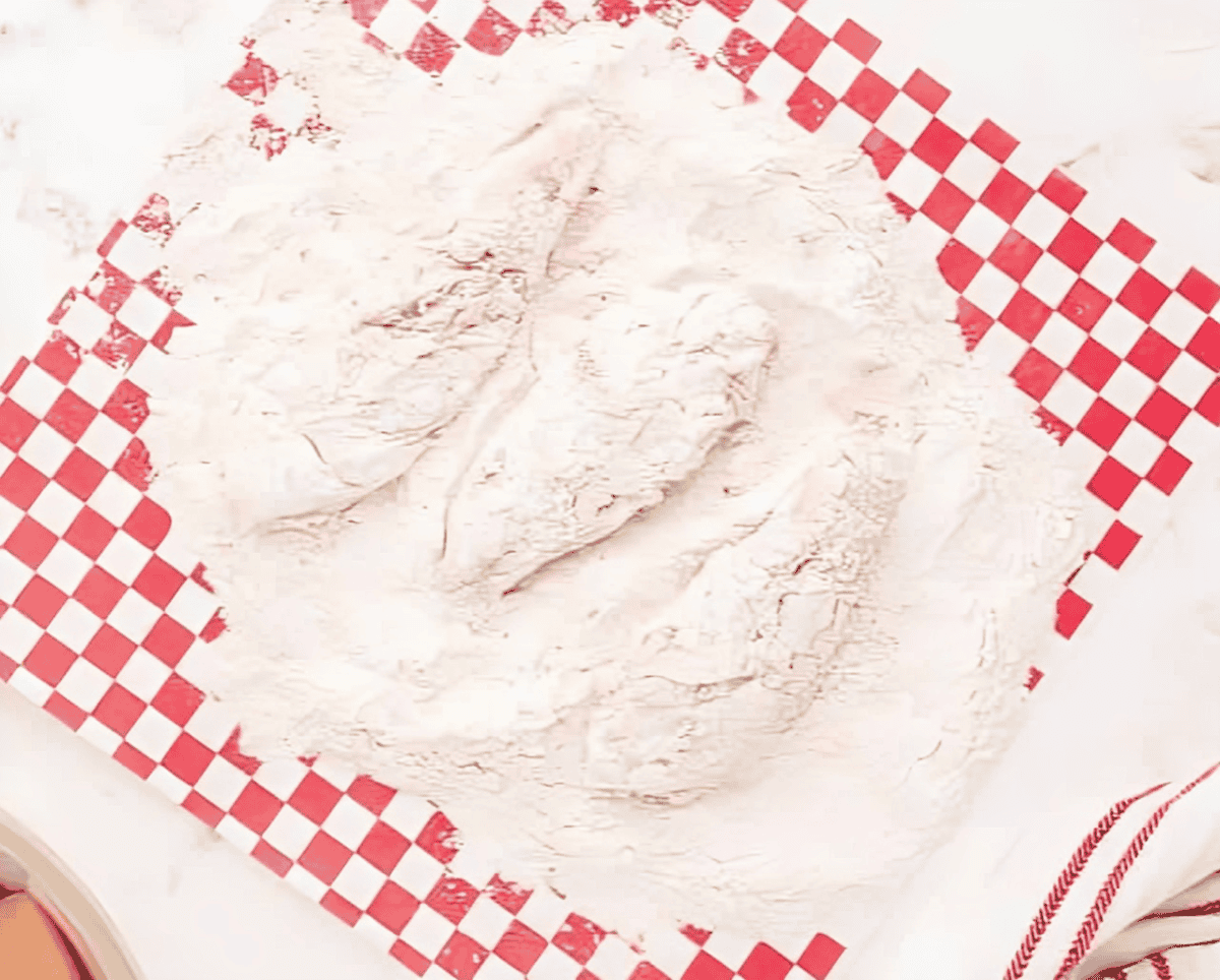 battered chicken tenders in a pile of flour.