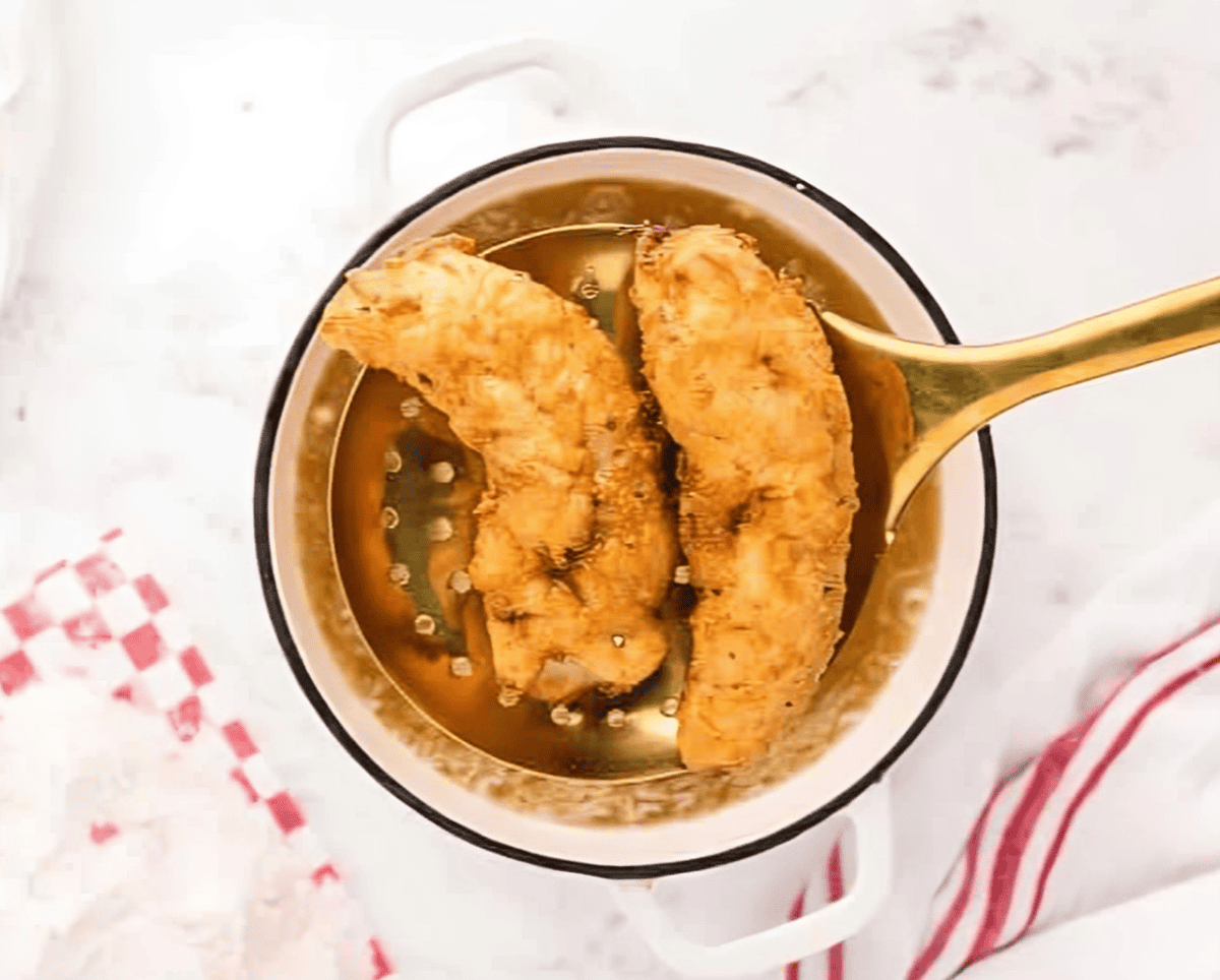 removing chicken fingers from hot oil with a strainer.