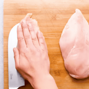 A knife slicing a pocket into a chicken breast for ham and cheese stuffed chicken.