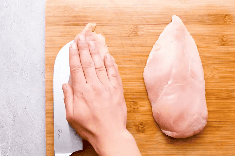 A knife slicing a pocket into a chicken breast for ham and cheese stuffed chicken.