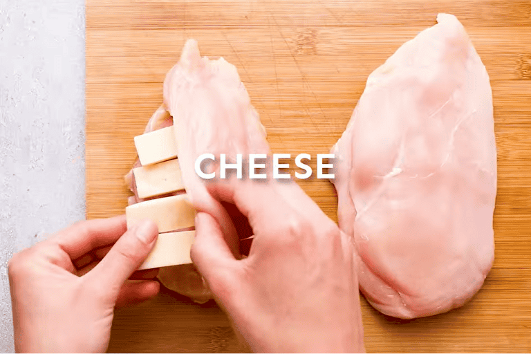 A hand stuffing chicken breast with ham and cheese.
