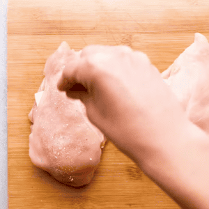 A hand sprinkling seasoning over ham and cheese stuffed chicken breast.