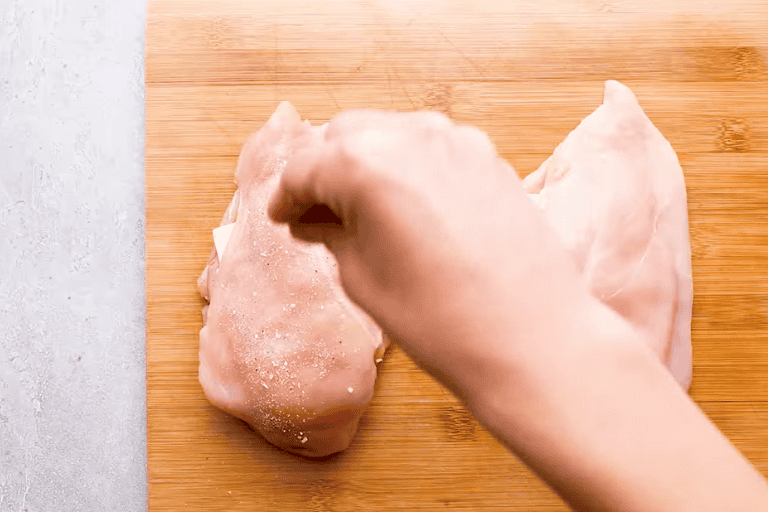 A hand sprinkling seasoning over ham and cheese stuffed chicken breast.