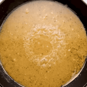 Broth for ham and cheese stuffed chicken in a skillet.