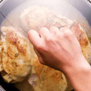 A hand placing a lid over a skillet with ham and cheese stuffed chicken.