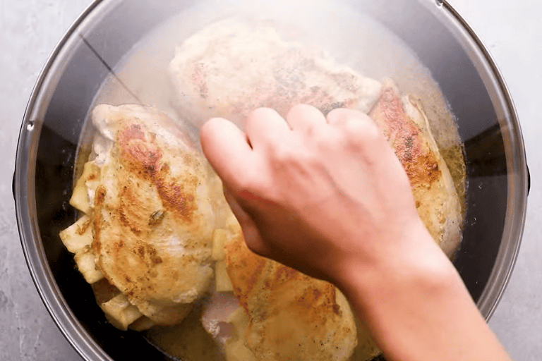 A hand placing a lid over a skillet to cook ham and cheese stuffed chicken.