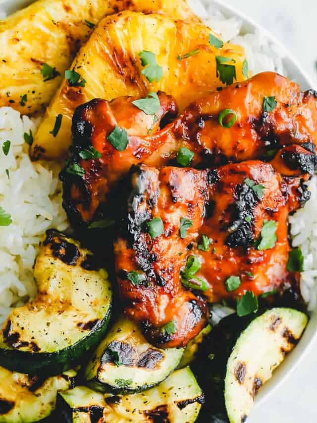 huli huli chicken served on a plate with rice, and grilled pineapples and cucumber