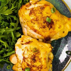two air fryer ranch chicken thighs on a blue plate with arugula and green onions.