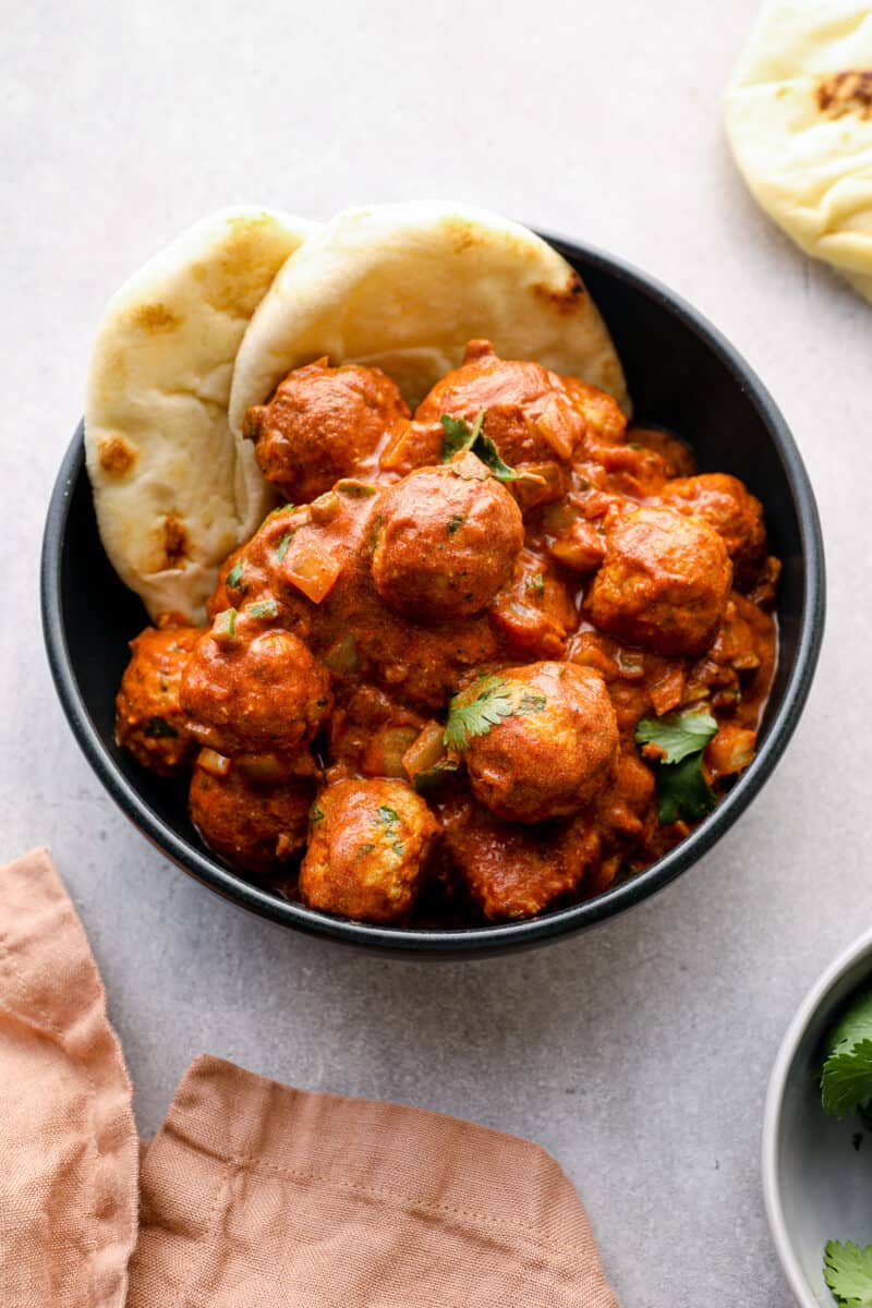 black bowl of butter chicken meatballs with naan