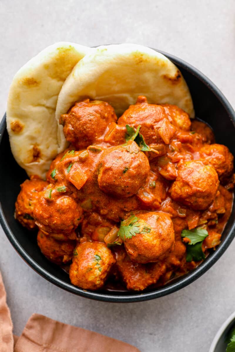 up close black bowl bowl of butter chicken meatballs with naan