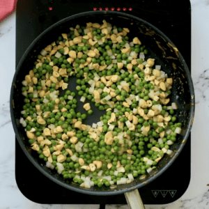 Cashews and peas sizzling in a frying pan.