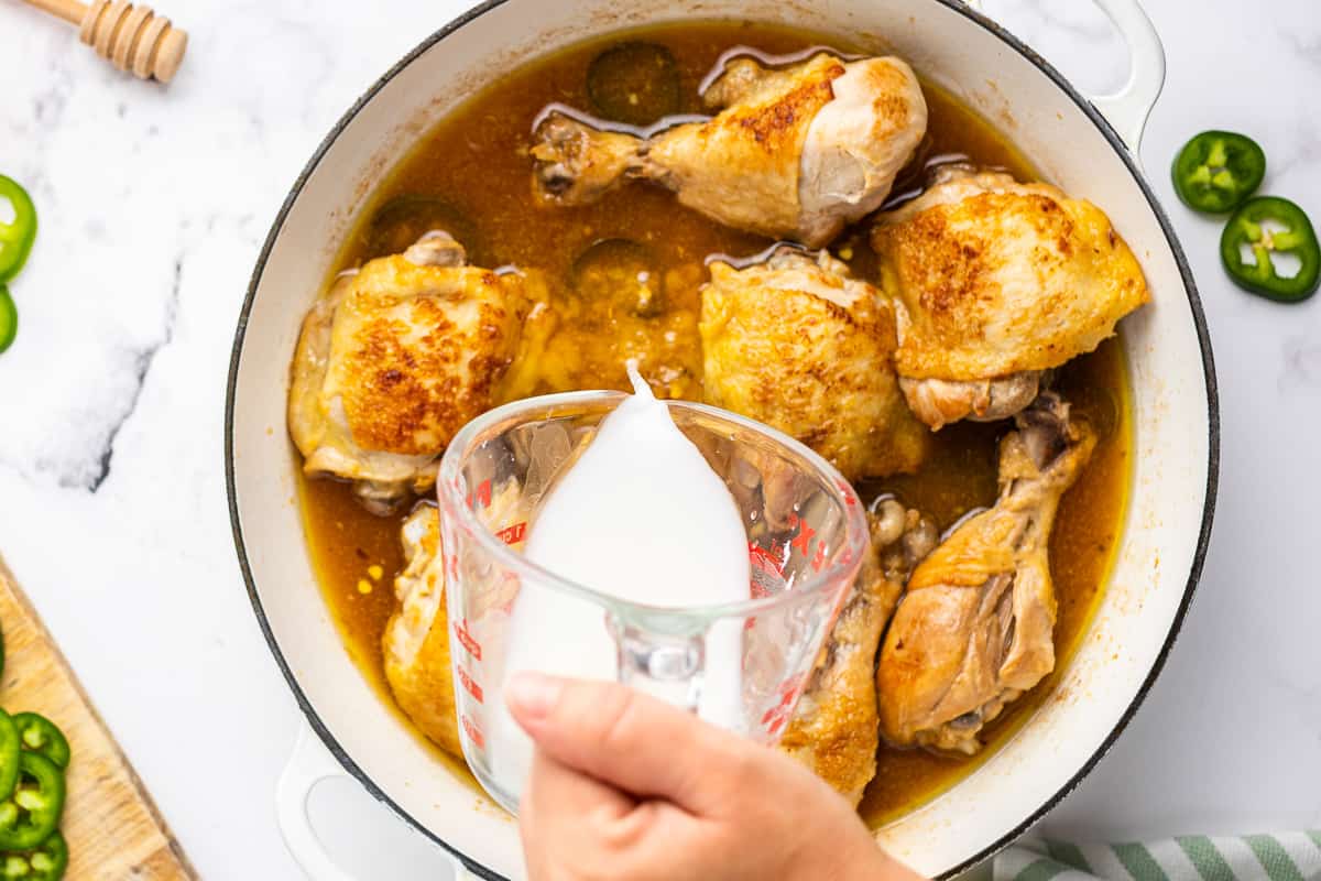 chicken adobo in a skillet with a cornstarch slurry being poured in.