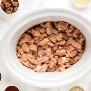 raw chicken chunks in a slow cooker.