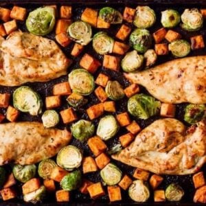 cooked chicken breasts, sweet potatoes, and brussels sprouts on a sheet pan.