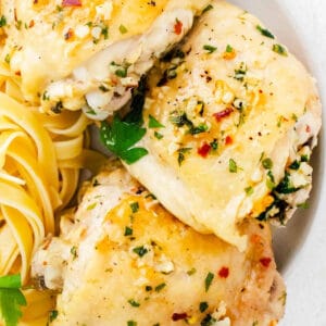 closeup of three instant pot garlic parmesan chicken thighs on a plate with pasta.
