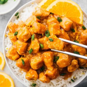 chopsticks lifting a piece of crockpot orange chicken from a bowl with rice.