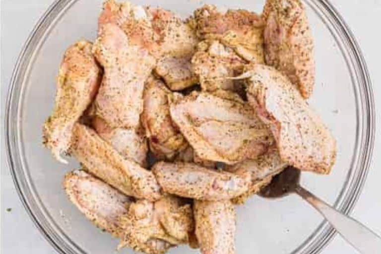 Chicken wings tossed in seasoning for garlic parmesan wings in a bowl.