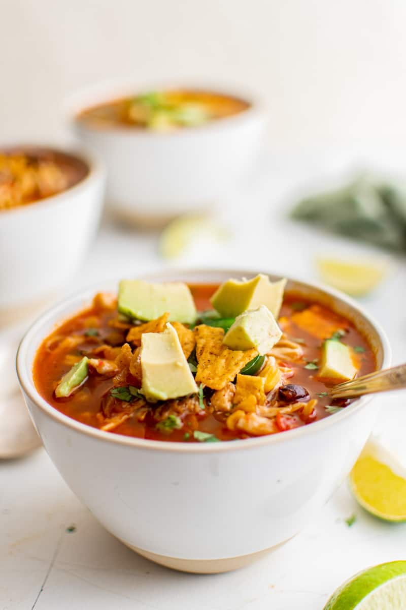 chicken taco soup topped with avocado chunks in a white bowl