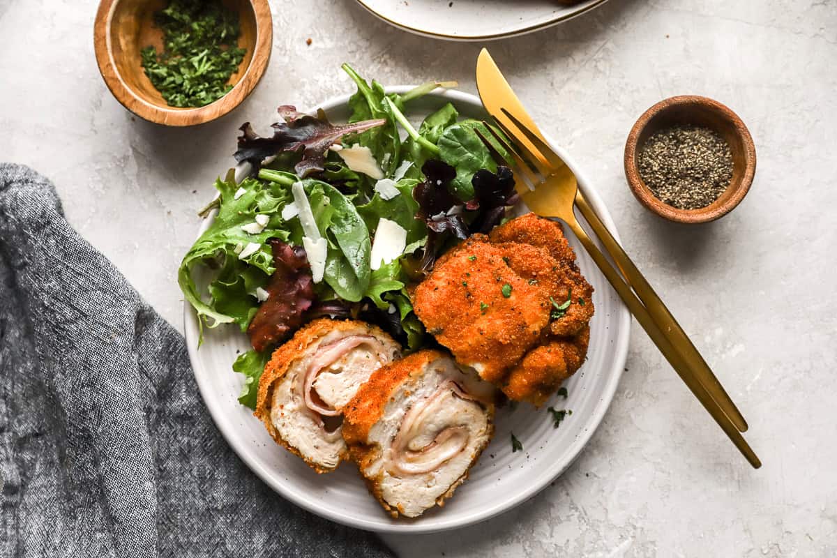 a sliced serving of chicken cordon bleu on a white plate with salad greens.