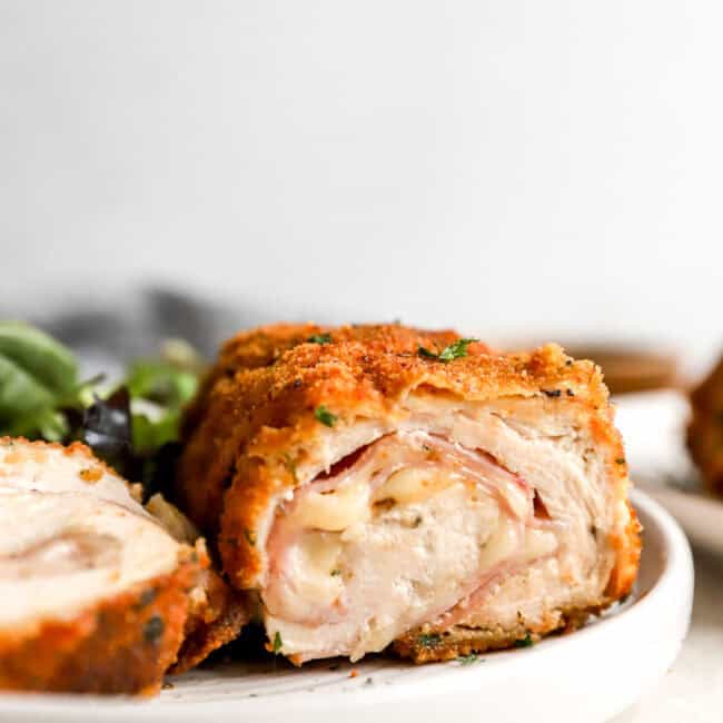 side view of a sliced serving of chicken cordon blue on a white plate showing the filling oozing out.