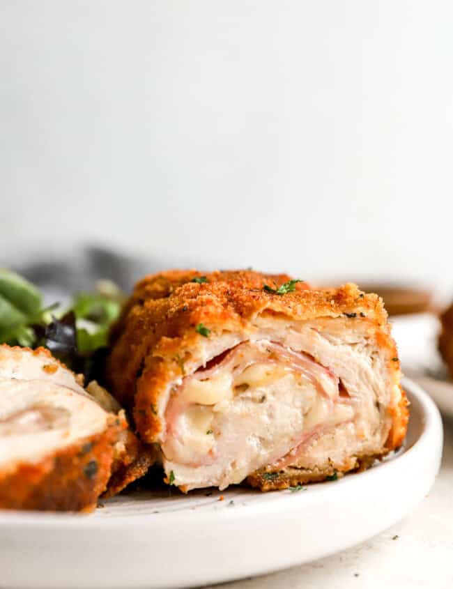 side view of a sliced serving of chicken cordon blue on a white plate showing the filling oozing out.