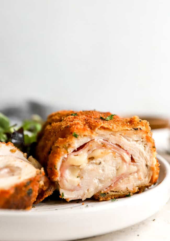 side view of a sliced serving of chicken cordon blue on a white plate showing the filling oozing out.