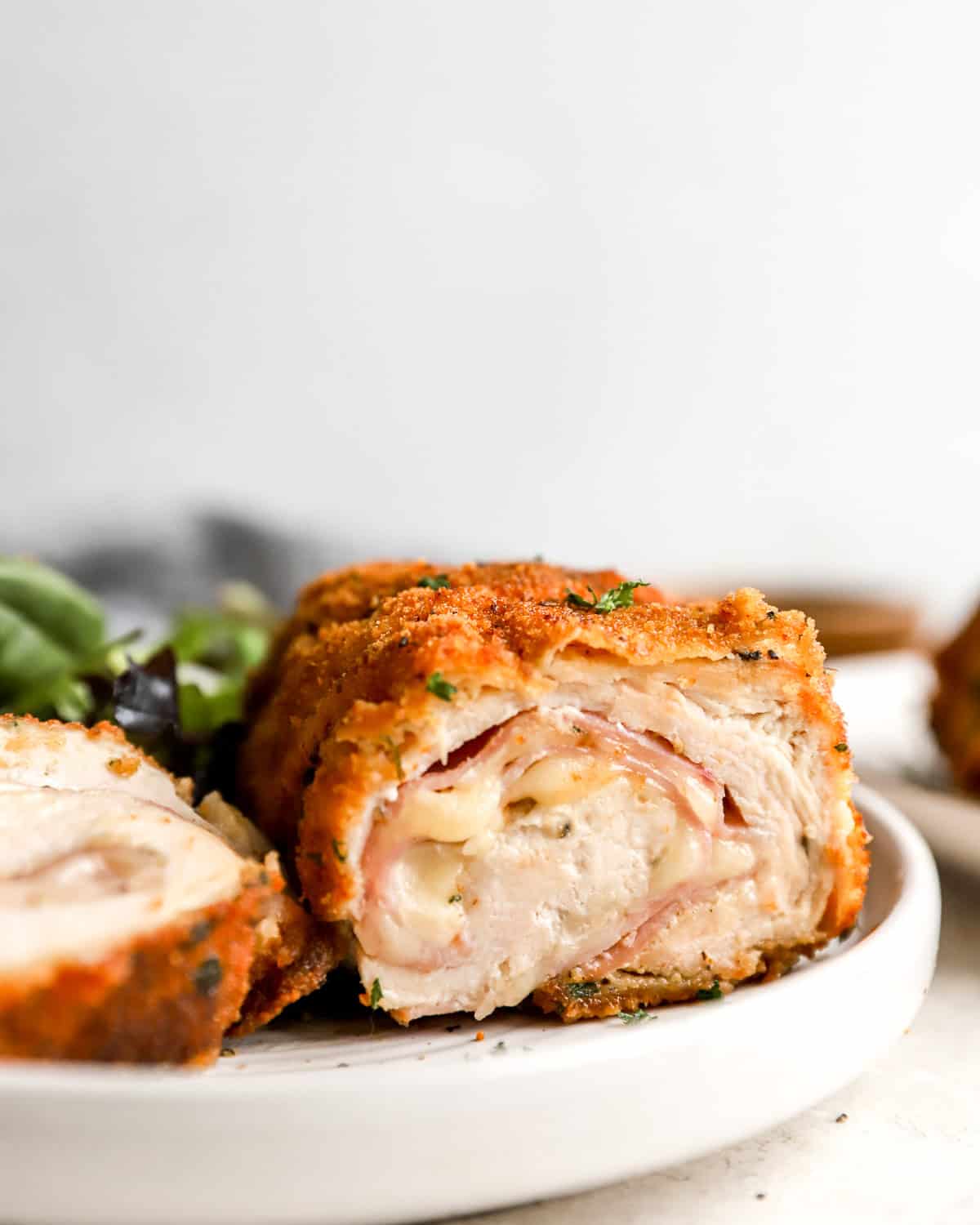 side view of a sliced serving of chicken cordon blue on a white plate showing the filling oozing out.