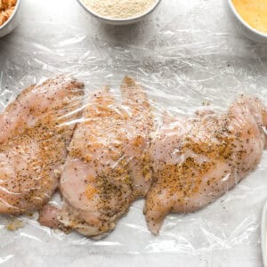 seasoned pounded chicken breasts under plastic wrap.