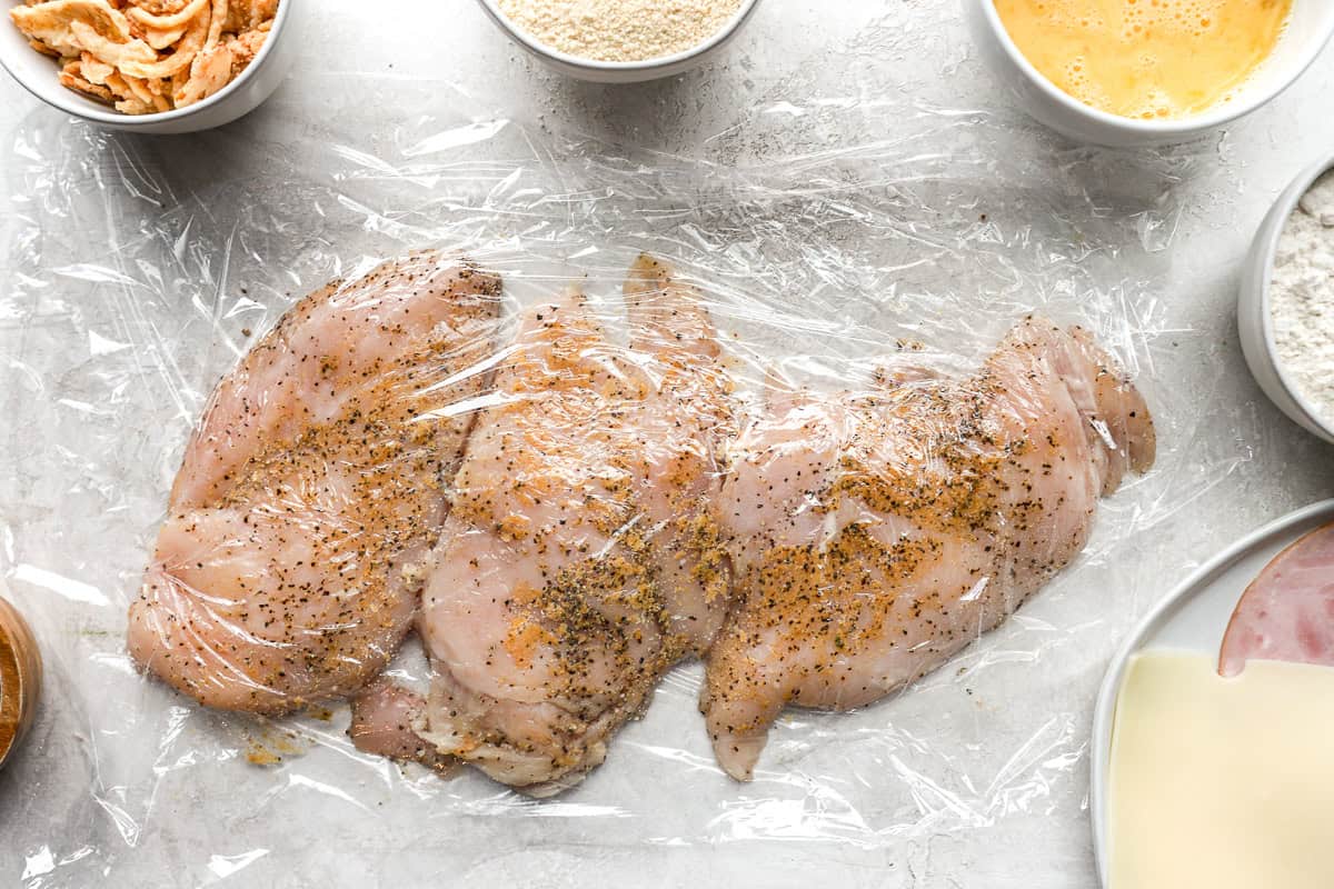 seasoned pounded chicken breasts under plastic wrap.