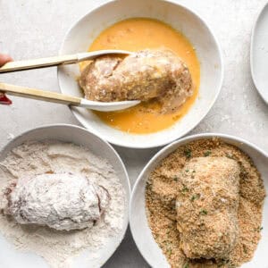 dipping rolled stuffed chicken breasts in flour, egg, and breadcrumbs with tongs.