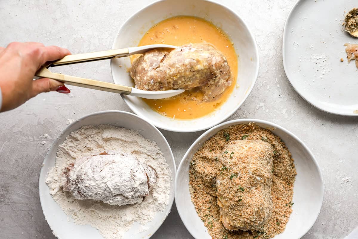 dipping rolled stuffed chicken breasts in flour, egg, and breadcrumbs with tongs.