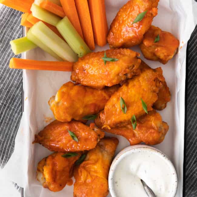 overhead image of honey buffalo chicken wings on a serving tray with sliced carrots and celery and dressing in a small bowl