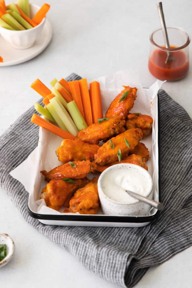 honey buffalo chicken wings on a serving tray with sliced carrots and celery and dressing in a small bowl