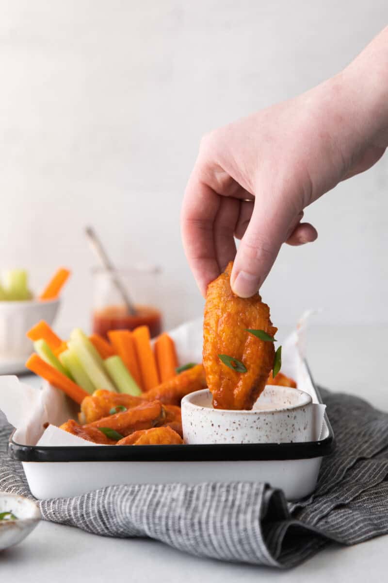 hand dipping a honey buffalo chicken wing into dressing