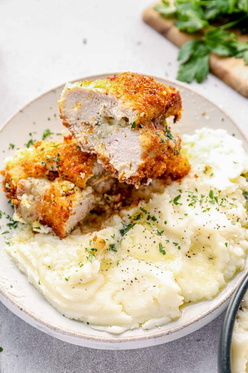 cheesy garlic stuffed chicken breast cut in half on a plate with mashed potatoes