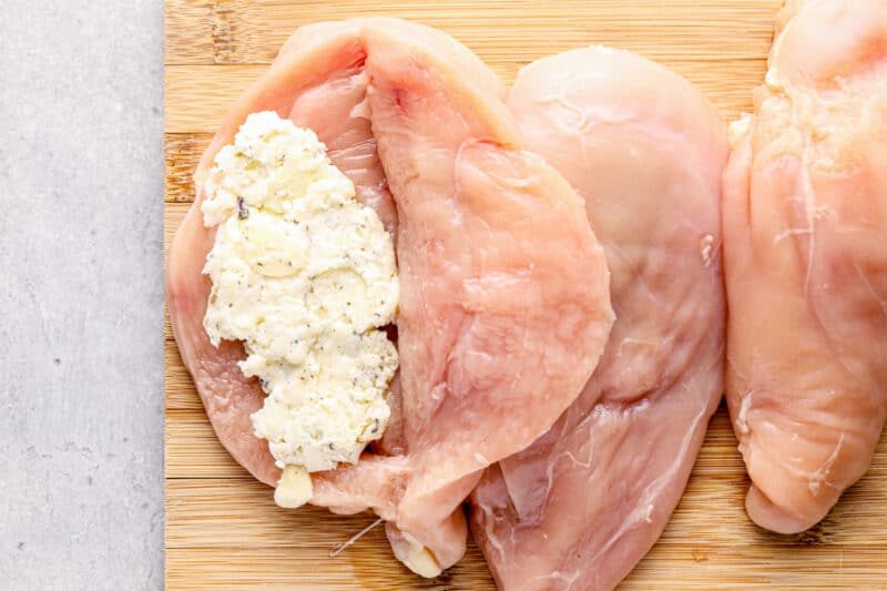 raw chicken breasts slit open and filled with garlic cheese mixture on a wood cutting board