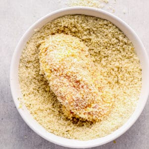 chicken breast in bowl of breadcrumbs and parmesan